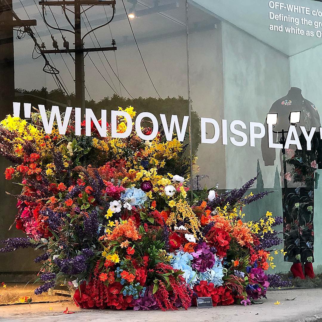 Oversized artificial flower window display in bright red, yellow, purple and blue blooms outside a boutique
