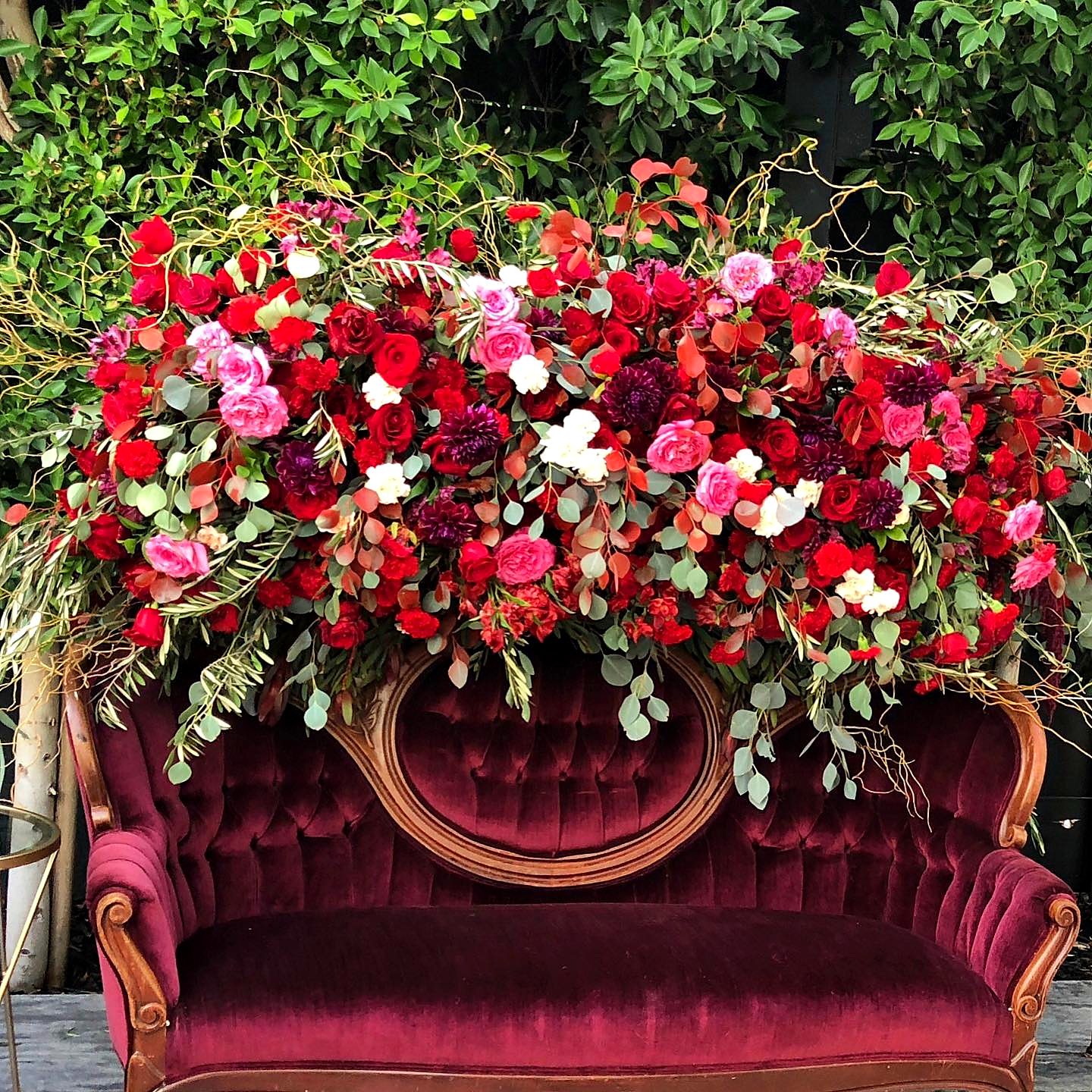 Oversized red and pink floral arrangement above a burgundy velvet sofa
