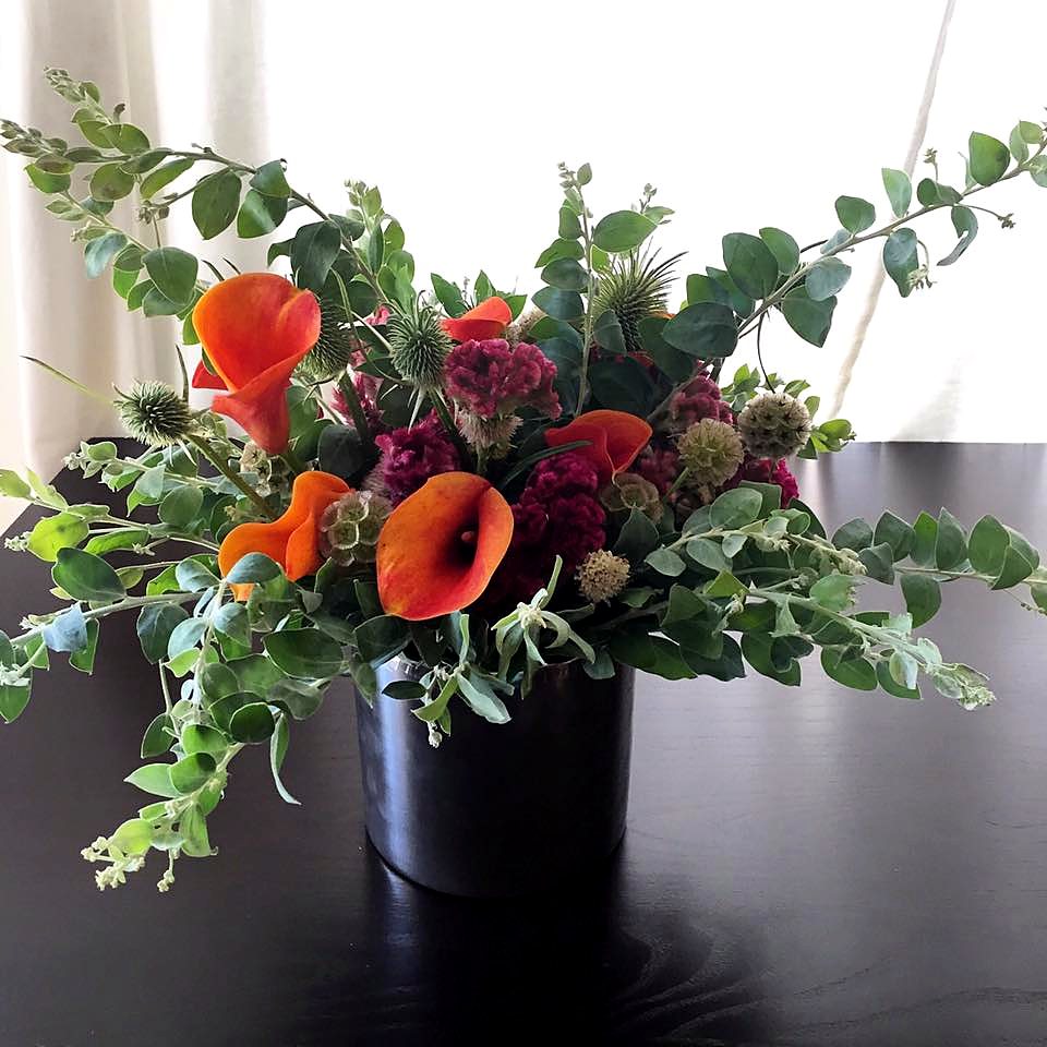 Orange calla lilies, burgundy celosia and eucalyptus in a dark vase