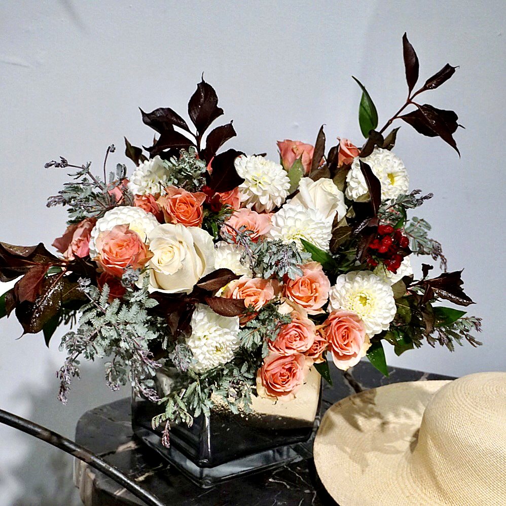 Peach and white roses, white dahlias and burgundy foliage in a mirrored glass cube