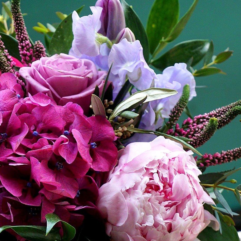 Close view of a pink peony, magenta hydrangea, lavender sweet pea and pink veronica against a teal wall