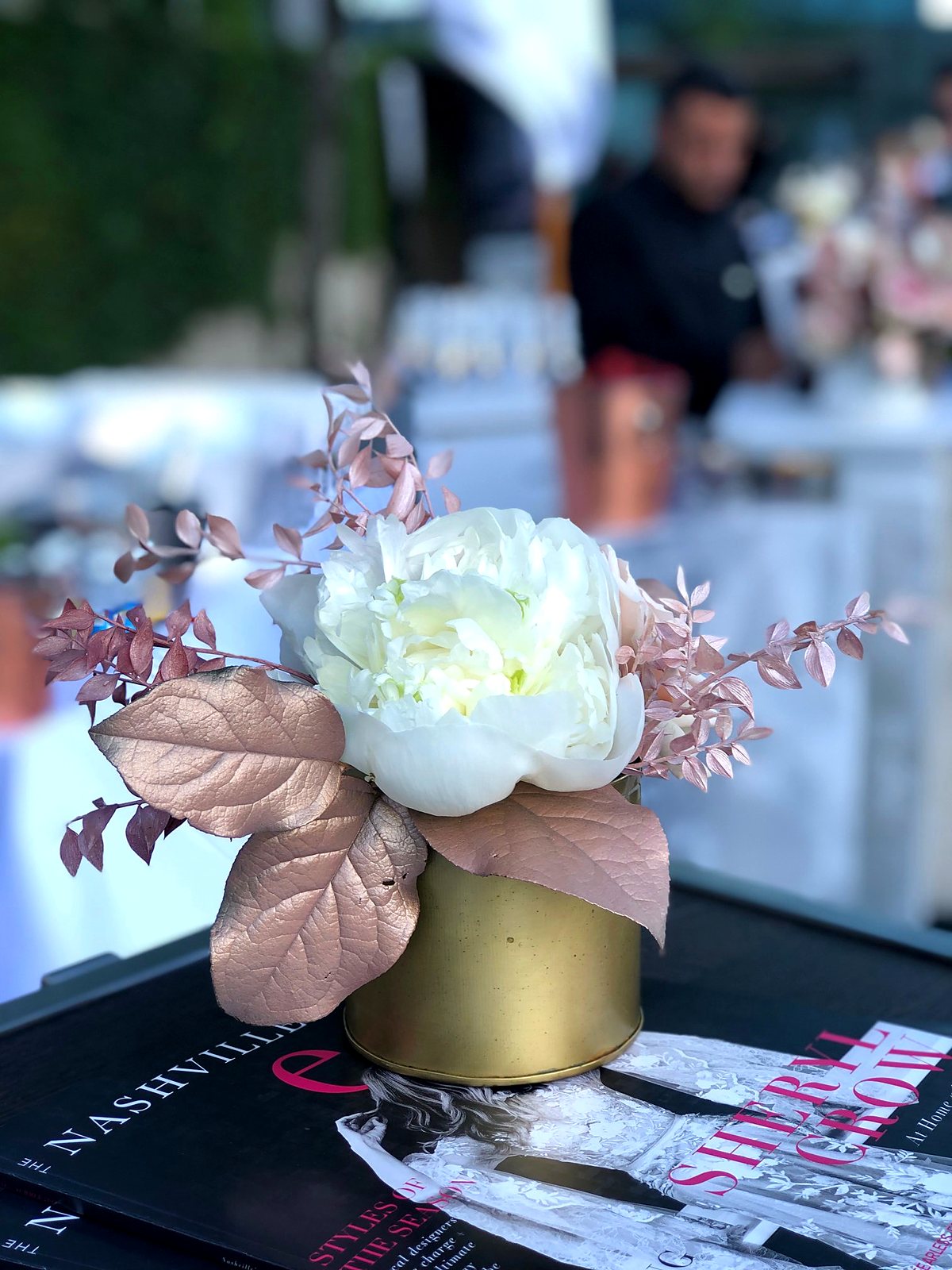 White peony with rose gold foliage in a small gold vase on a stack of The Nashville Edit magazines
