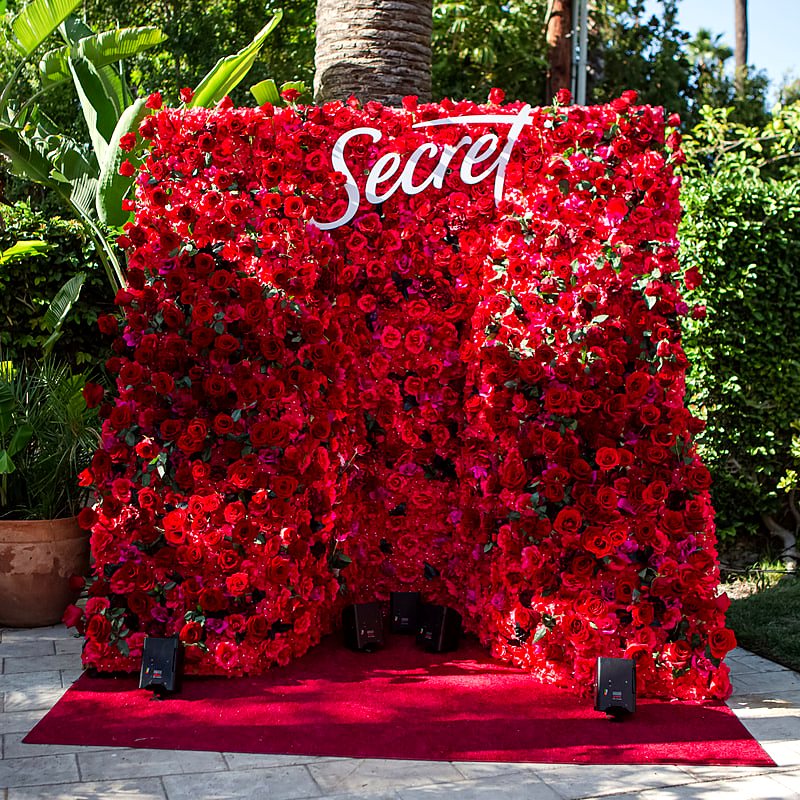 Red rose flower wall with a white script brand logo at an outdoor activation