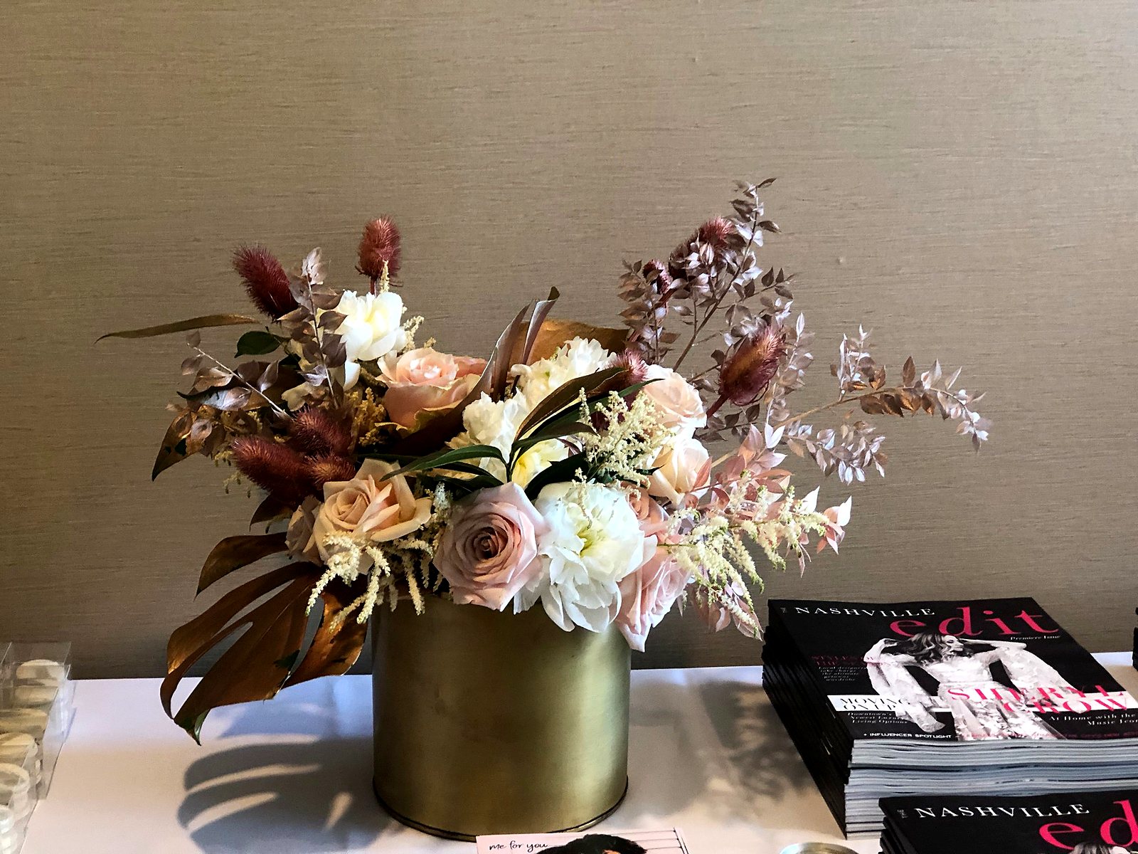 Blush roses, white peonies and rose gold and bronze foliage in a gold vase next to The Nashville Edit premiere issue