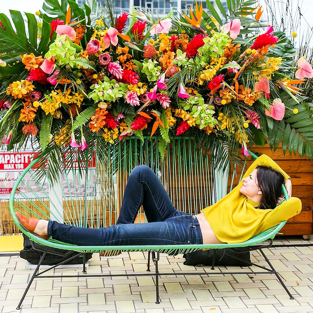 Oversized tropical flower installation of bird of paradise, anthurium and orchids behind a lounge chair