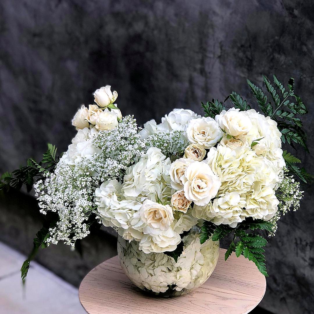 White hydrangea, roses and baby's breath in a glass bowl on a round stool