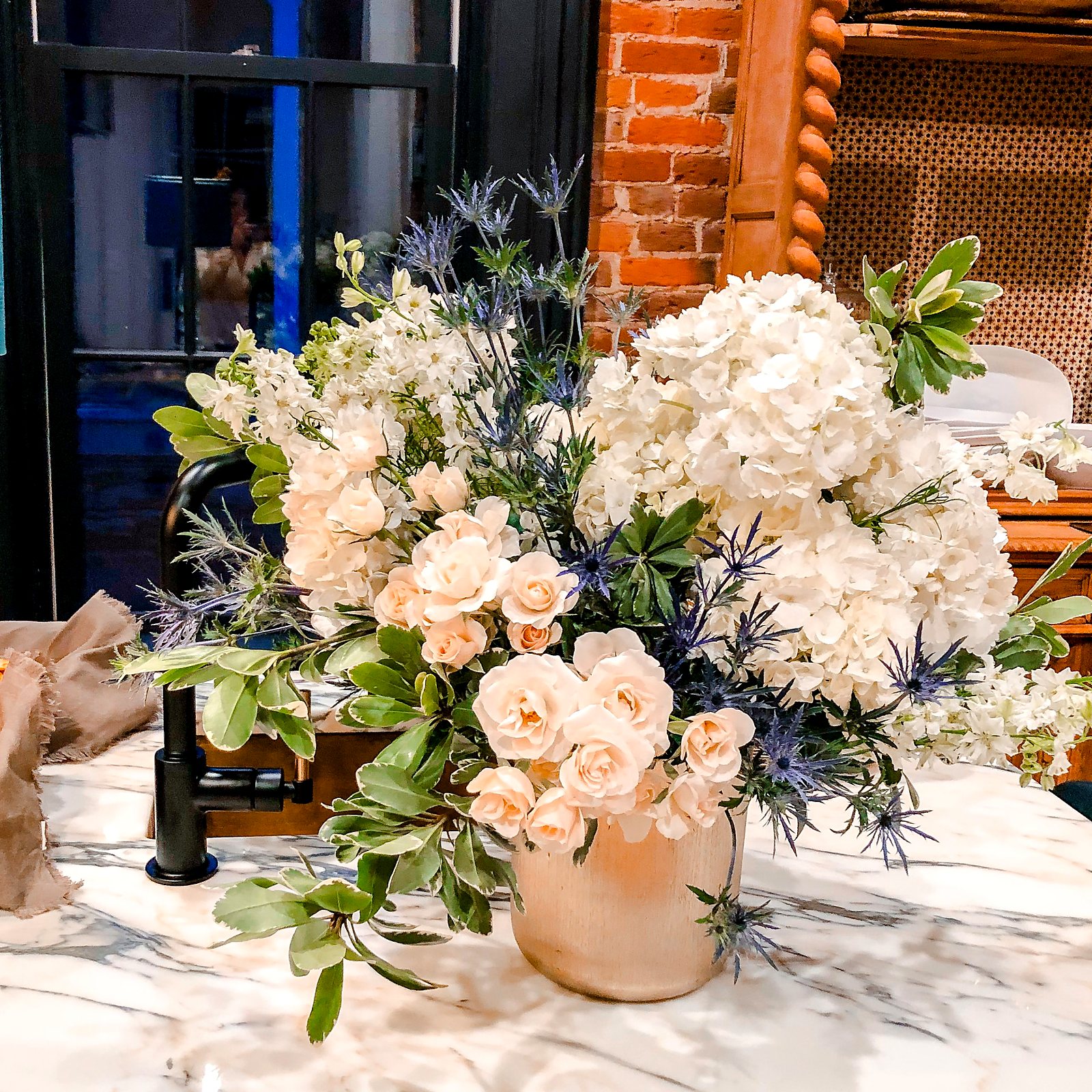 White hydrangea, stock and spray roses with blue thistle on a marble counter